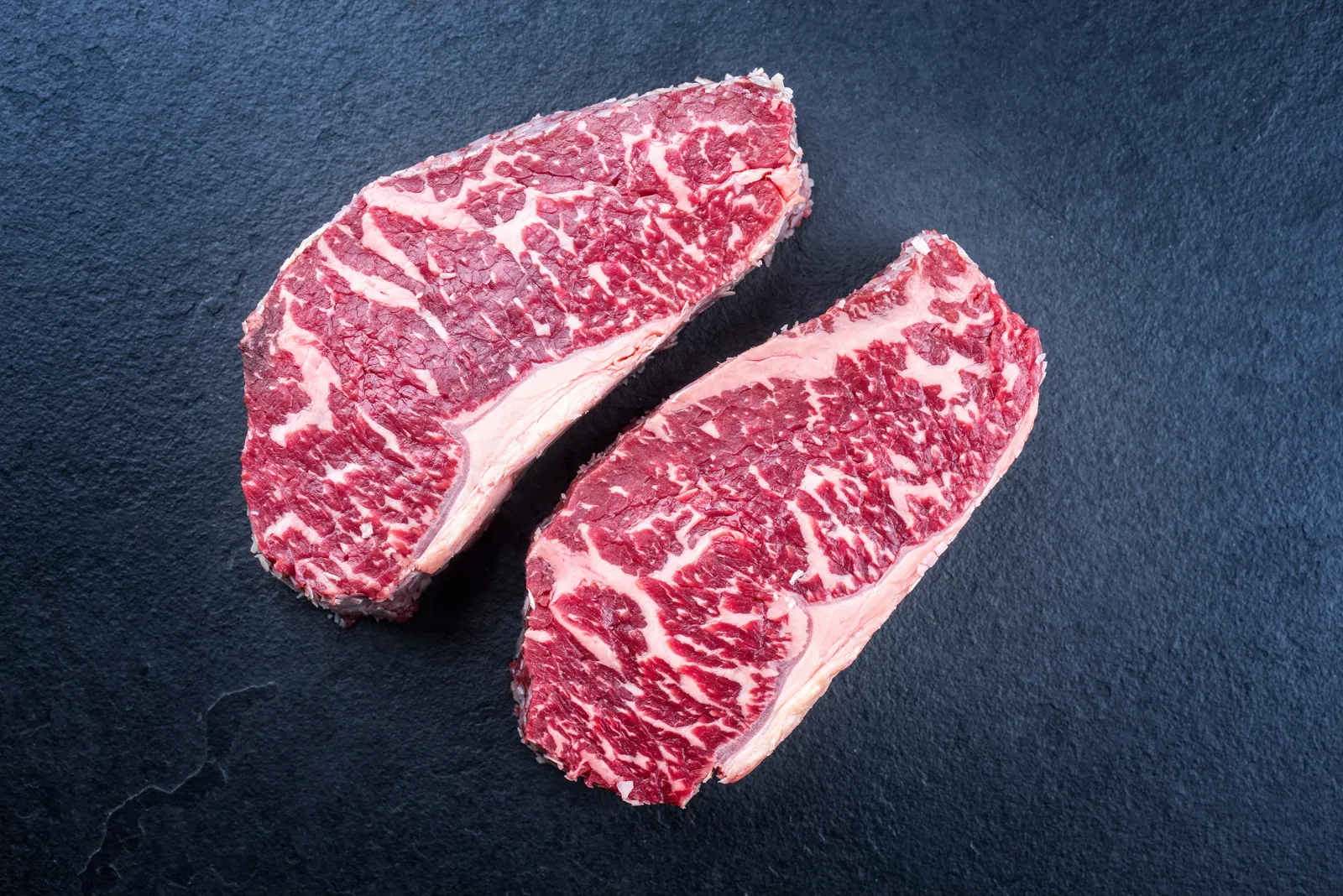 Two raw Wagyu steaks on slate